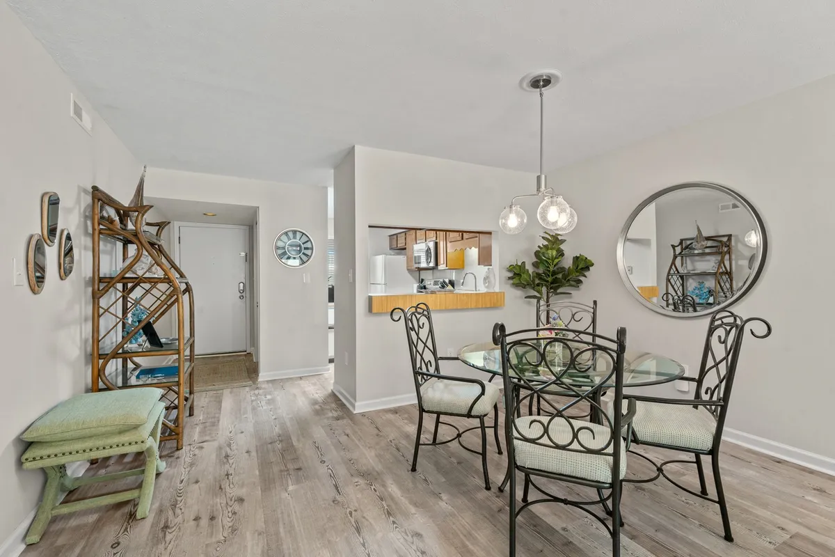 An inviting dining area with a central dining table, decorative mirror, rattan chair, and a kitchen pass-through, creating a seamless flow between kitchen and dining. The setting is cozy and ideal for shared meals and conversations.