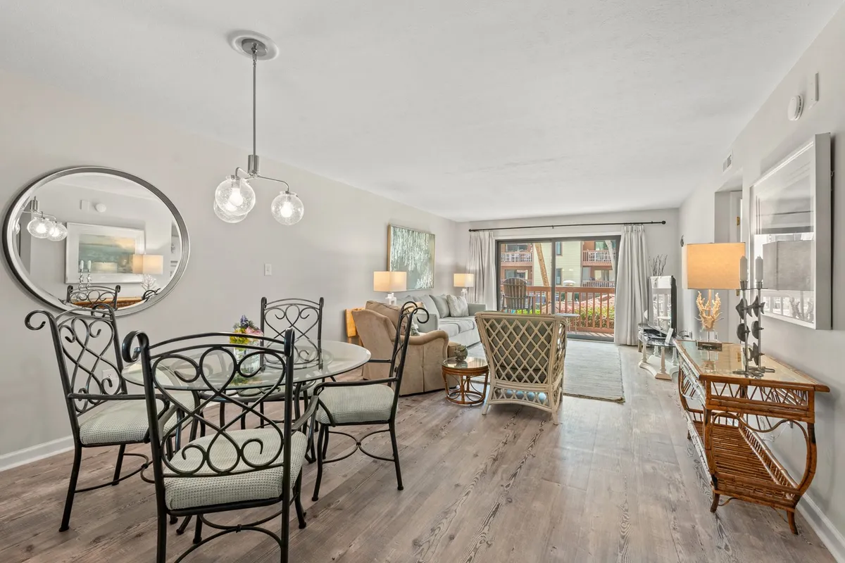 A combined living and dining area with a dining table, sofa, and a large window letting in abundant sunlight. Decorative touches like a mirror and coastal artwork add warmth and personality, while the window view enhances the sense of openness.