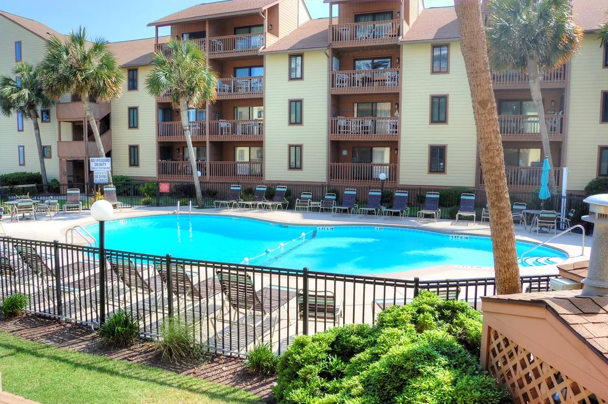 A vibrant exterior view of the Anchorage II's inviting swimming pool surrounded by palm trees and balconies. The scene is lively and welcoming, with lounge chairs and a well-maintained pool deck perfect for both relaxation and recreation.