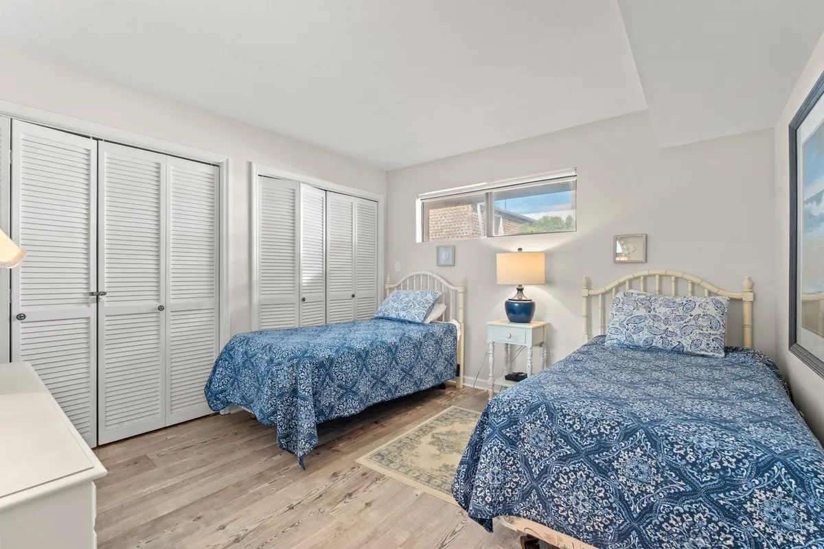 A cozy second bedroom with two twin beds dressed in blue-patterned bedding, a nightstand with a lamp and decorative accents, and large closet doors. The room radiates a peaceful, family-friendly vibe.