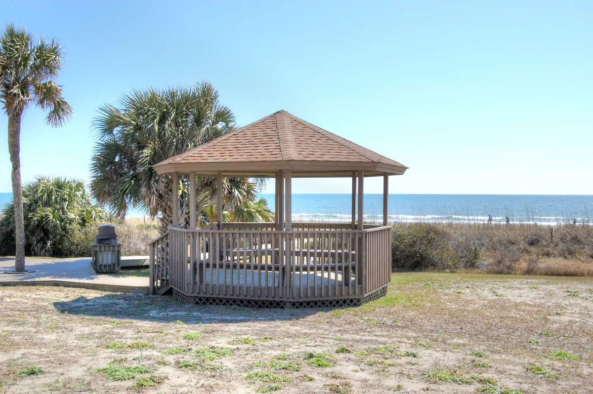 A charming gazebo sits among palm trees with a sweeping ocean view beyond. The area invites relaxation, picnics, and social gatherings, with the sea serving as a stunning backdrop. The mood is tranquil, perfect for unwinding after beach adventures or savoring quiet moments by the water.