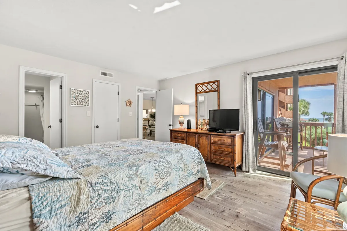 A serene bedroom featuring a large bed with a blue quilt, a wooden dresser, a spacious window offering plenty of natural light, and access to a private balcony. The overall decor is soothing and designed for comfort, perfect for restful nights.